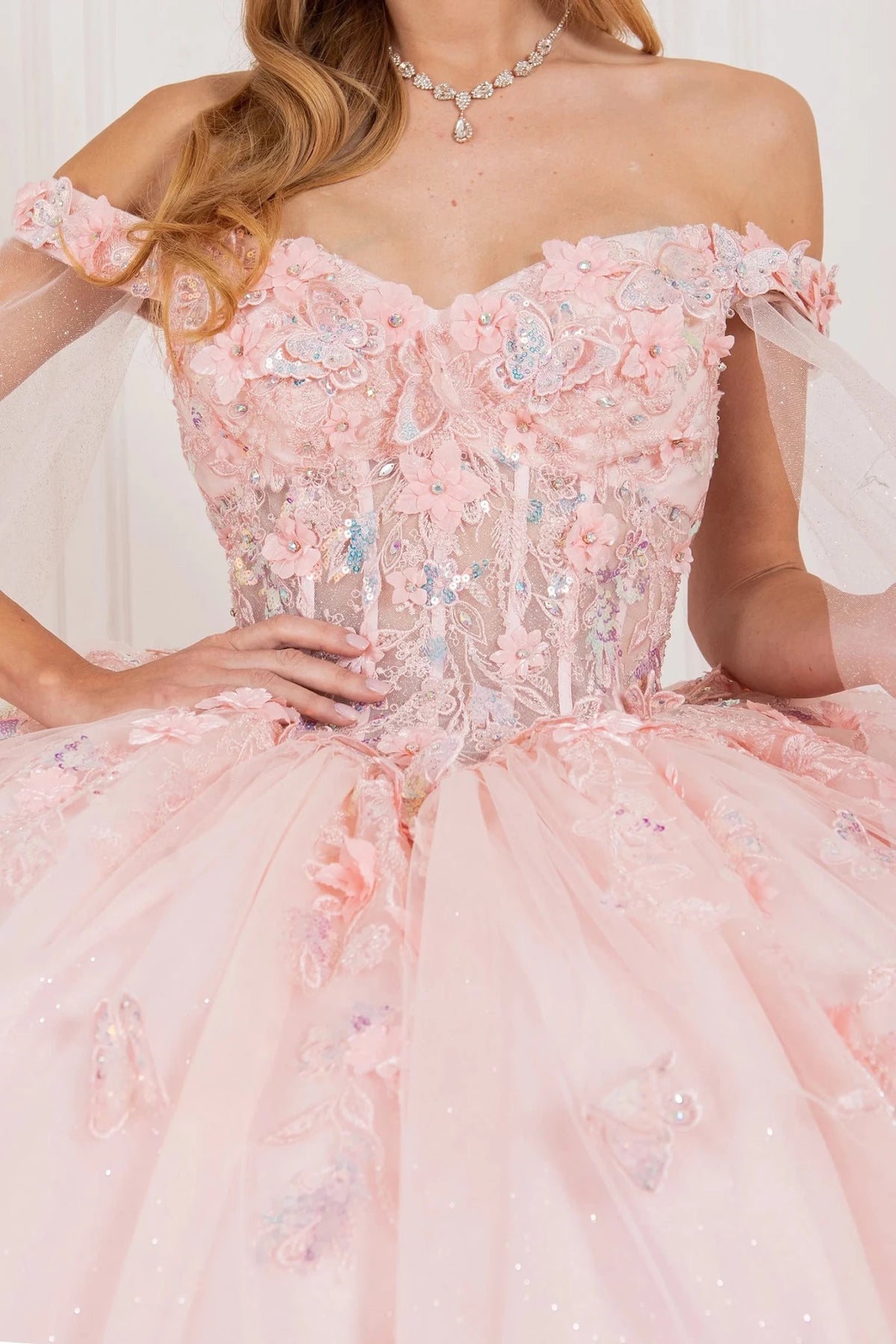 Butterfly appliqués shimmer across the Blush quinceañera dress's off-the-shoulder bodice.