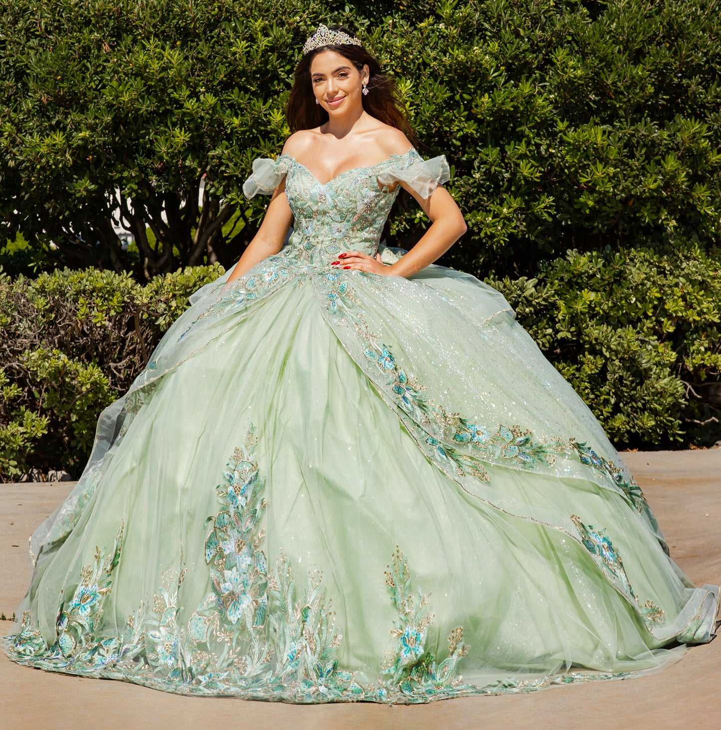 Woman in a green floral gown standing outdoors with greenery in the background