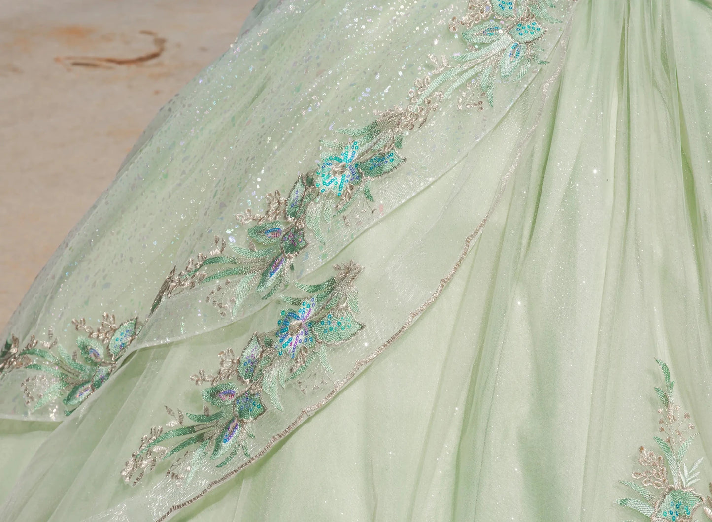 Light green fabric with floral embroidery and sequins on a neutral background