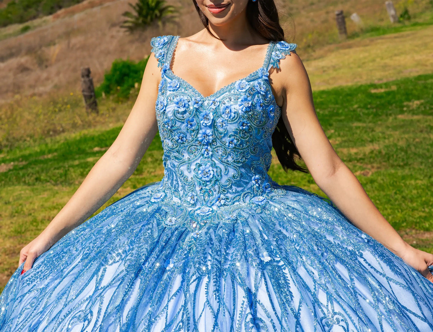 Front view of a woman wearing blue quinceanera ball gown with sequin detailing, ombre tulle skirt, and sweep train