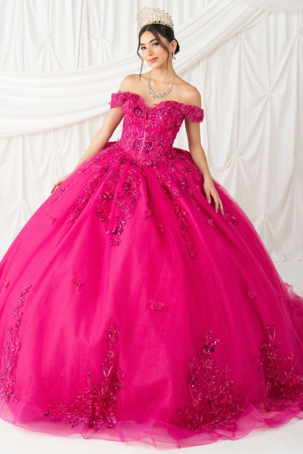 Shown in a front view, the Fuchsia quinceañera dress has off-shoulder floral bodice and butterfly appliques down the ball skirt.