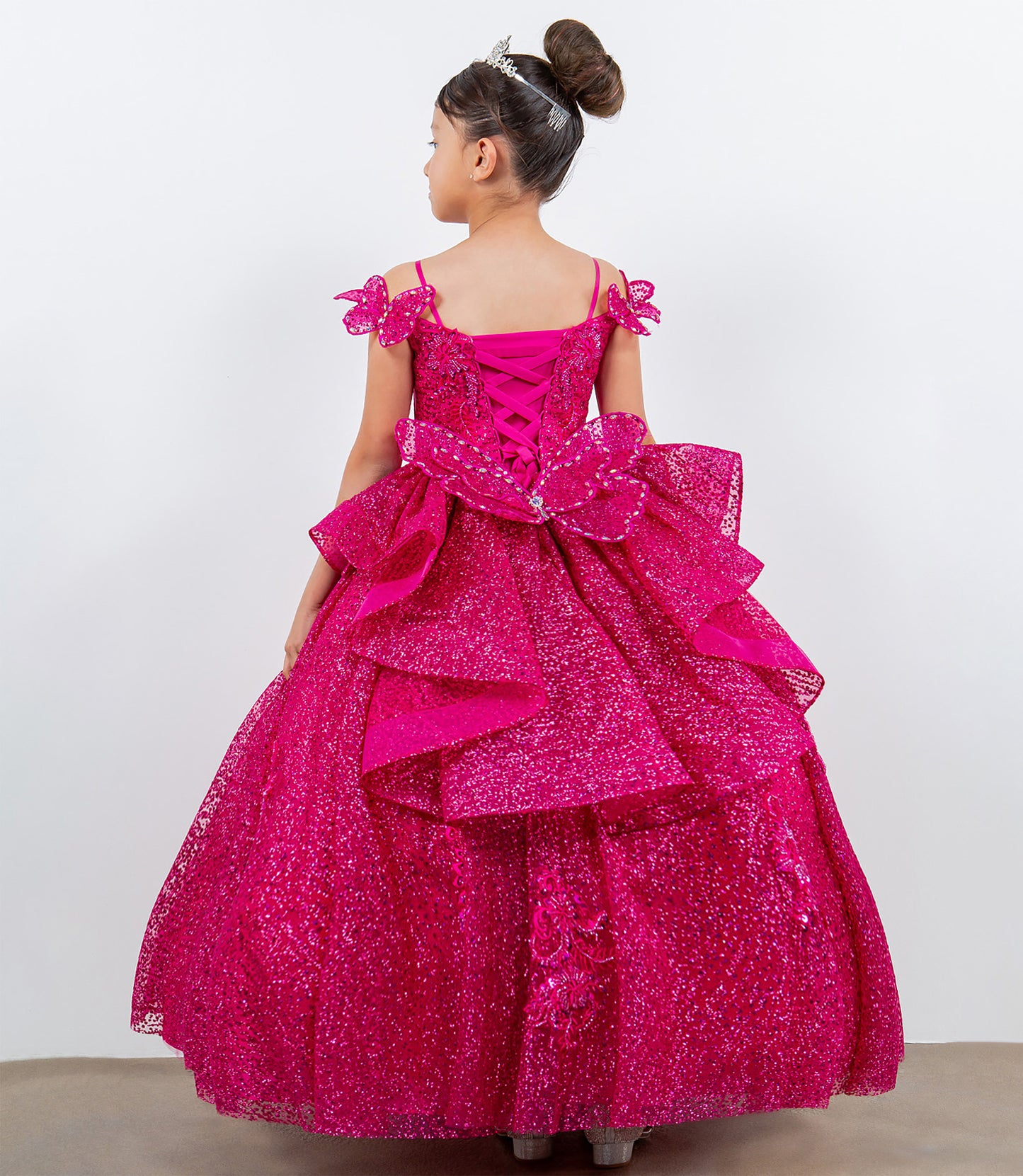 Young girl wearing a pink sparkly dress with ruffles on a white background