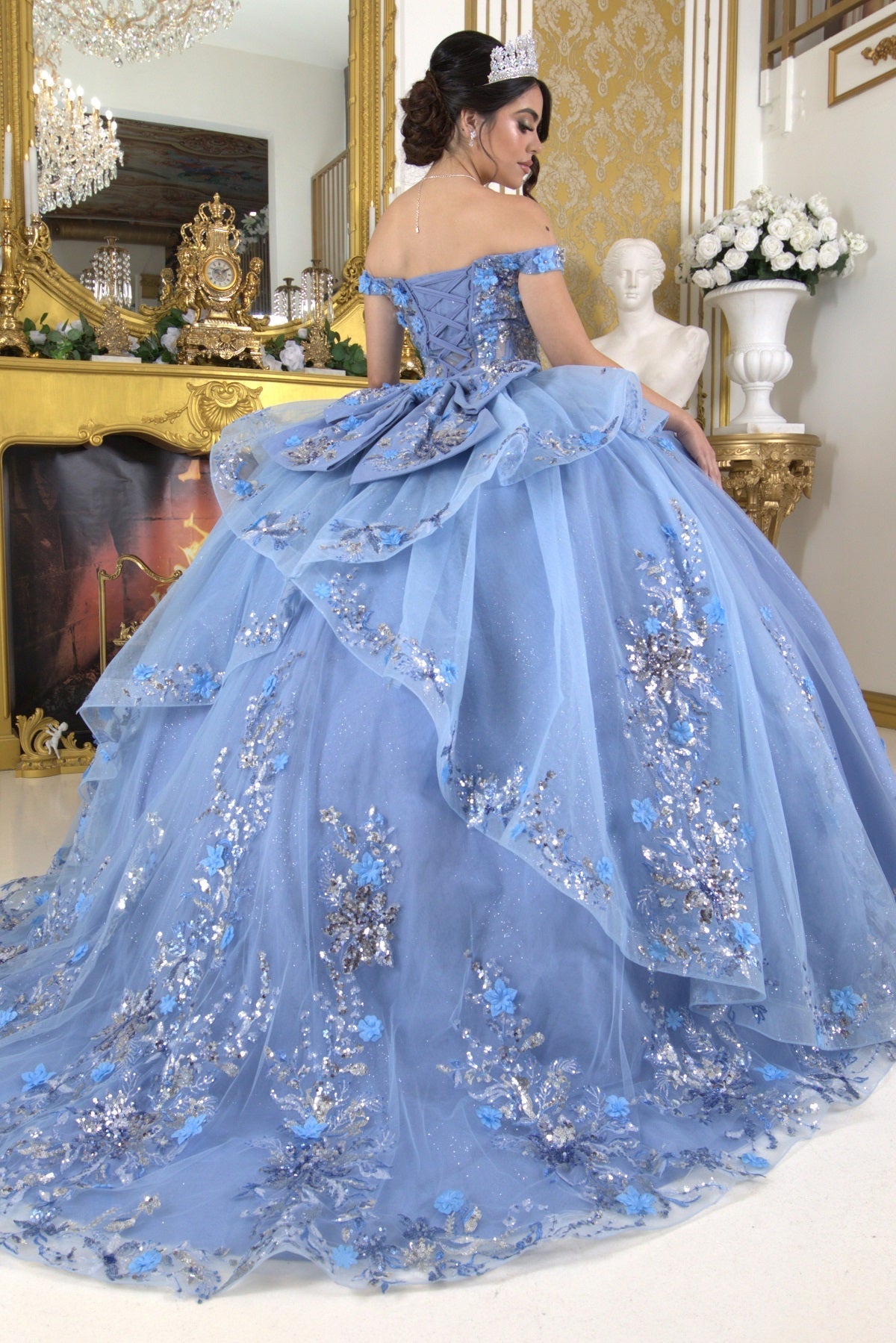 Rear view of a woman wearing blue quinceanera ball gown with seven-layer tulle skirt, floral beaded appliques, and lace-up detailing