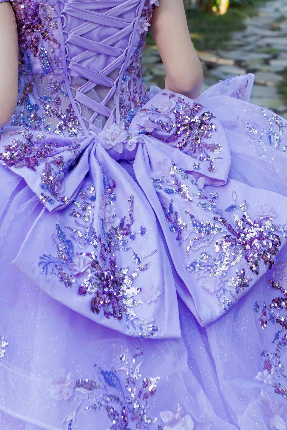 Detailed view highlights lilac quinceanera ball gown ribbon with floral beaded appliques and seven-layer tulle skirt.