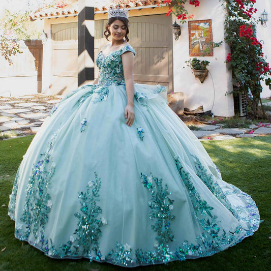 A girl wearing a sage green quinceañera ballgown with a sweetheart neckline, off-shoulder design, and a floral and beaded appliqué bodice, standing outdoors.