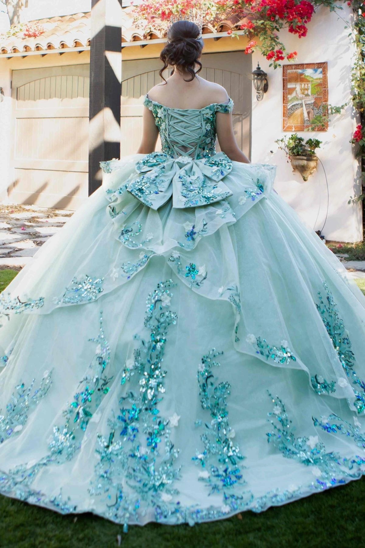Shown in a back view, the Sage quinceañera dress has lace-up back and floral bow over the layered ball skirt.