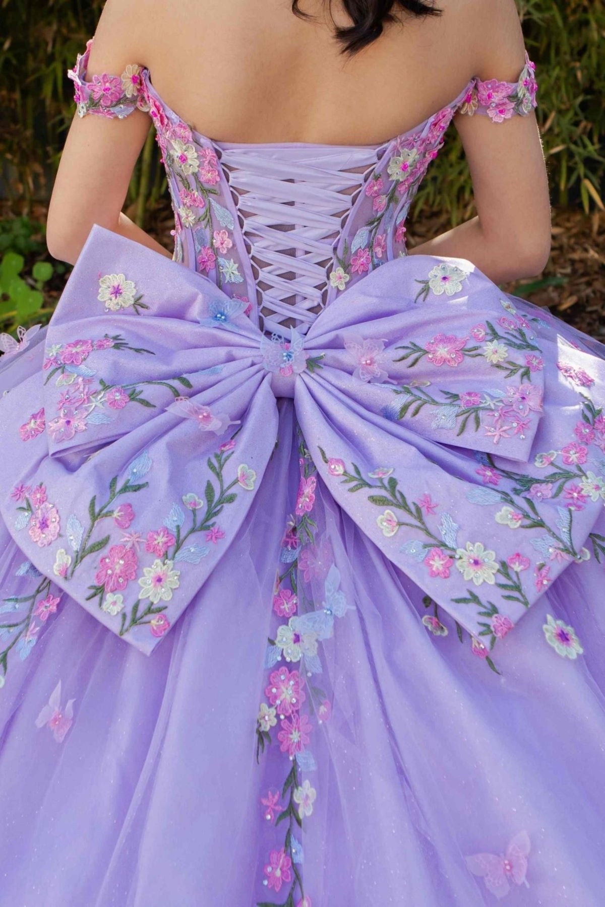 Back detail shows zoomed a lilac quinceanera ball gown with multicolor daisy embroidery, detachable bow, and lace-up train.