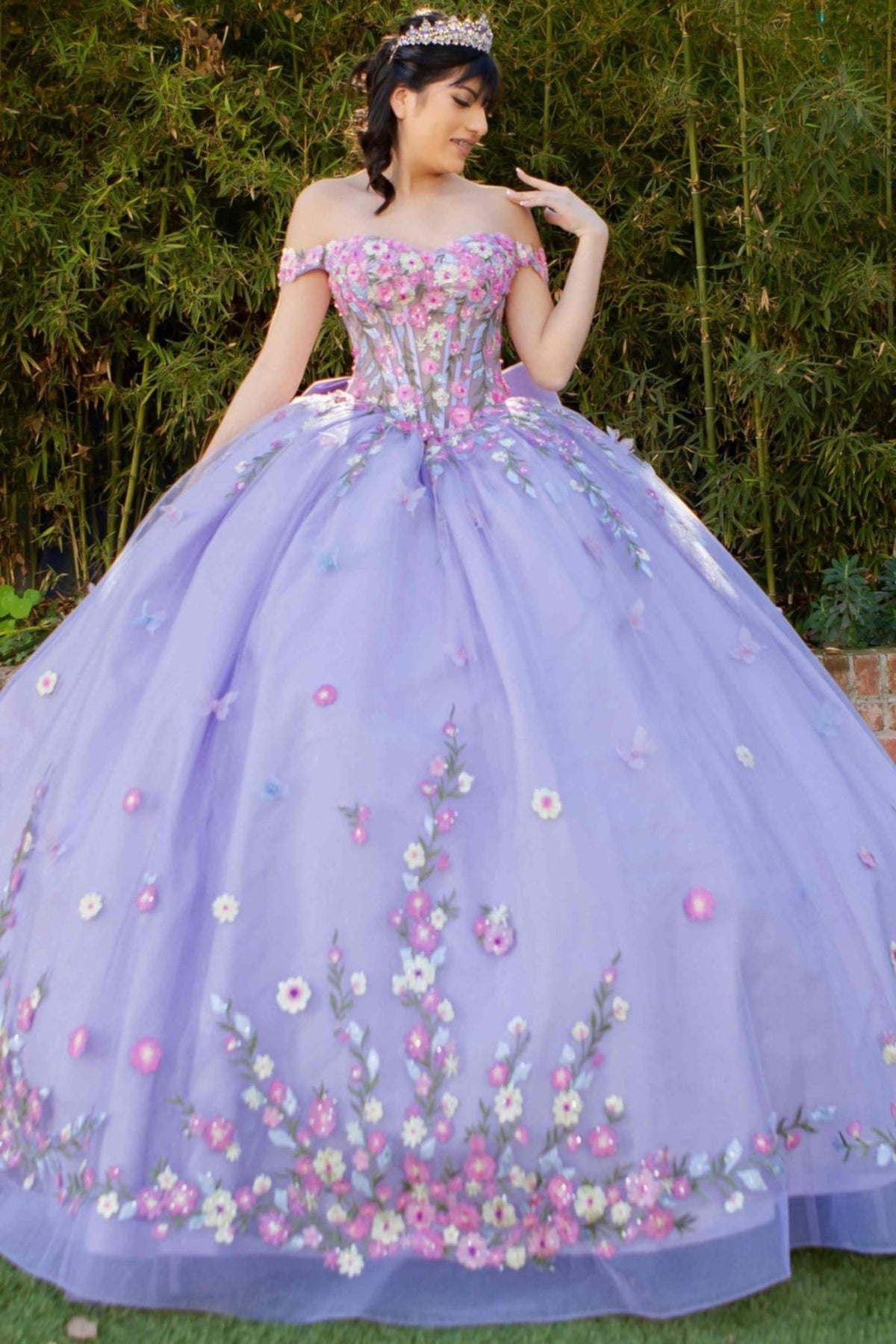 Skirt detail shows lilac quinceanera ball gown with multicolor daisy embroidery, detachable bow, and glitter tulle skirt.