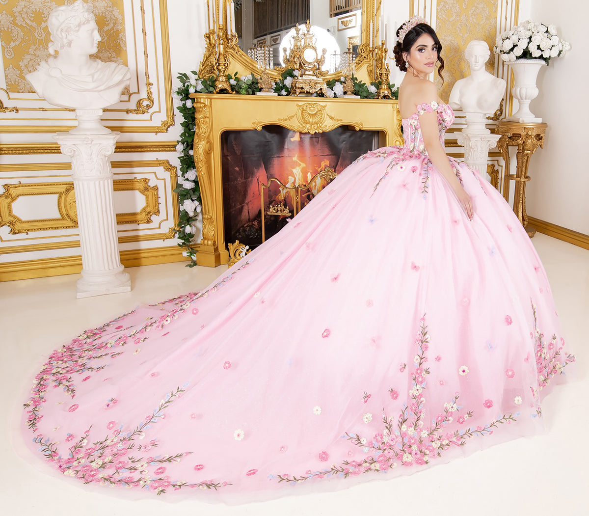 Side profile shows pink quinceanera ball gown with multicolor daisy embroidery, detachable bow, and rhinestone detailing.