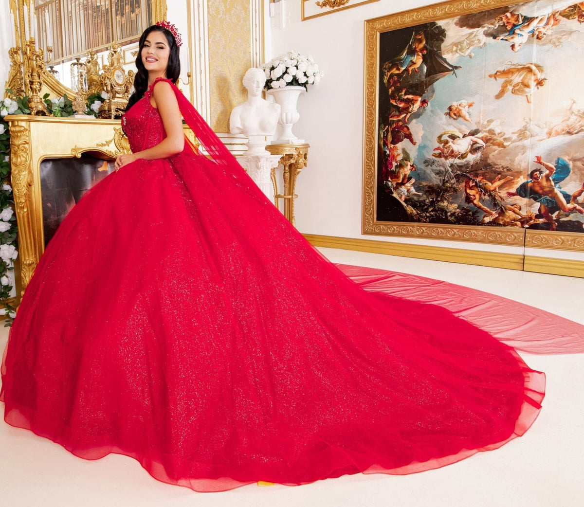 Profile view highlights red quinceanera ball gown with floral embellishments, central brooch, and flowing sheer cape.