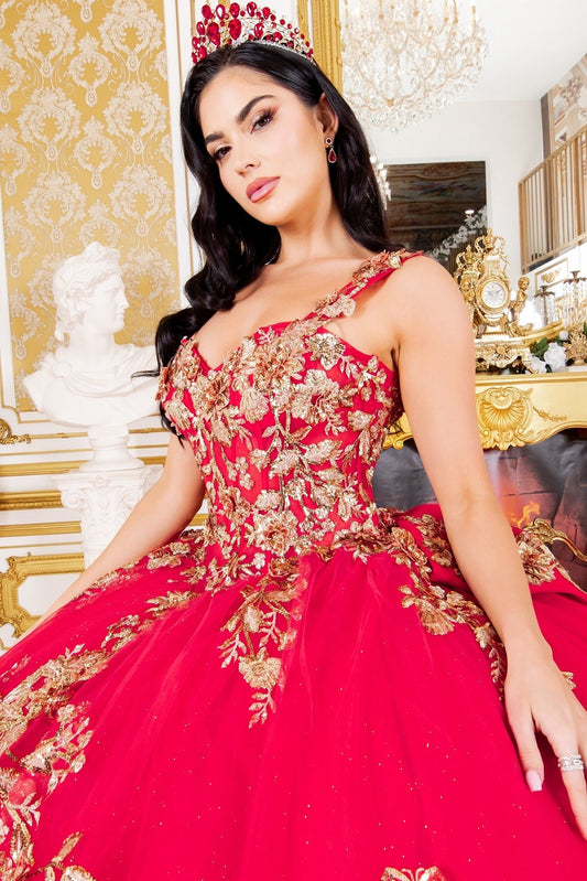 Woman standing front-facing in red ball gown with gold floral embroidery, voluminous skirt, fitted bodice, and matching crown in opulent indoor setting with chandelier and classical décor