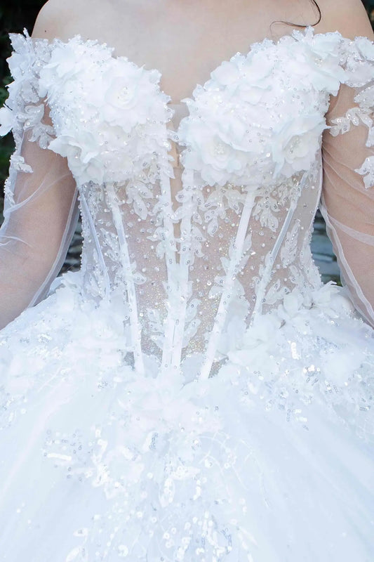 Zoomed front view of an off-white quinceanera dress highlighting lace appliques, beadwork bodice, floral details, and shimmering sequins