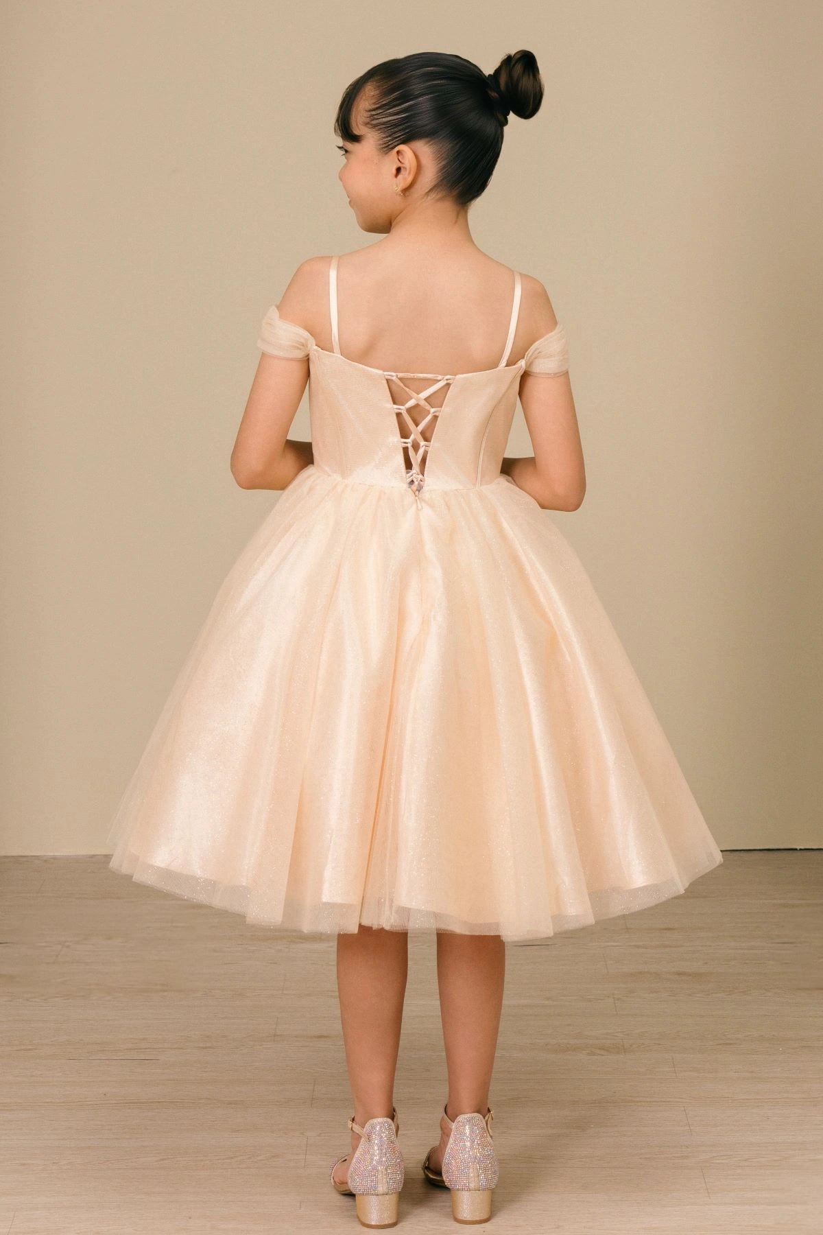 Presented in a back view, the Champagne girls formal dress has lace-up closure and thin straps above a tulle skirt.