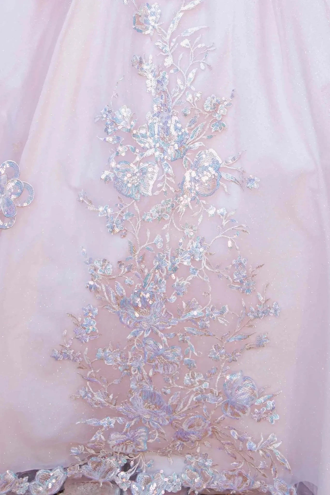 Skirt detail of a rose gold quinceanera dress with layered shimmering tulle fabric, scattered floral appliques, and chapel-length train