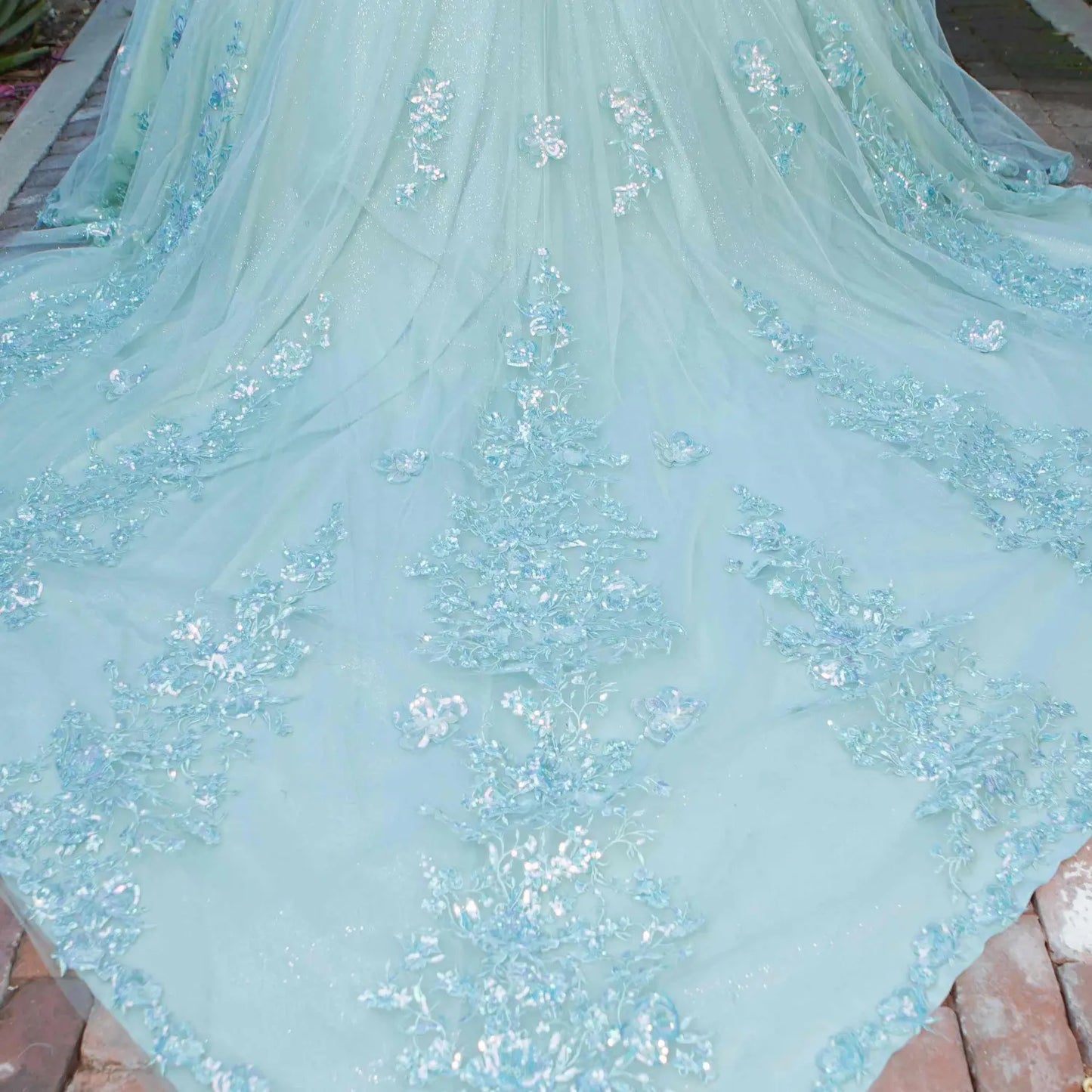 Skirt detail of a silver sage quinceanera dress with layered shimmering tulle fabric, scattered floral appliques, and chapel-length train