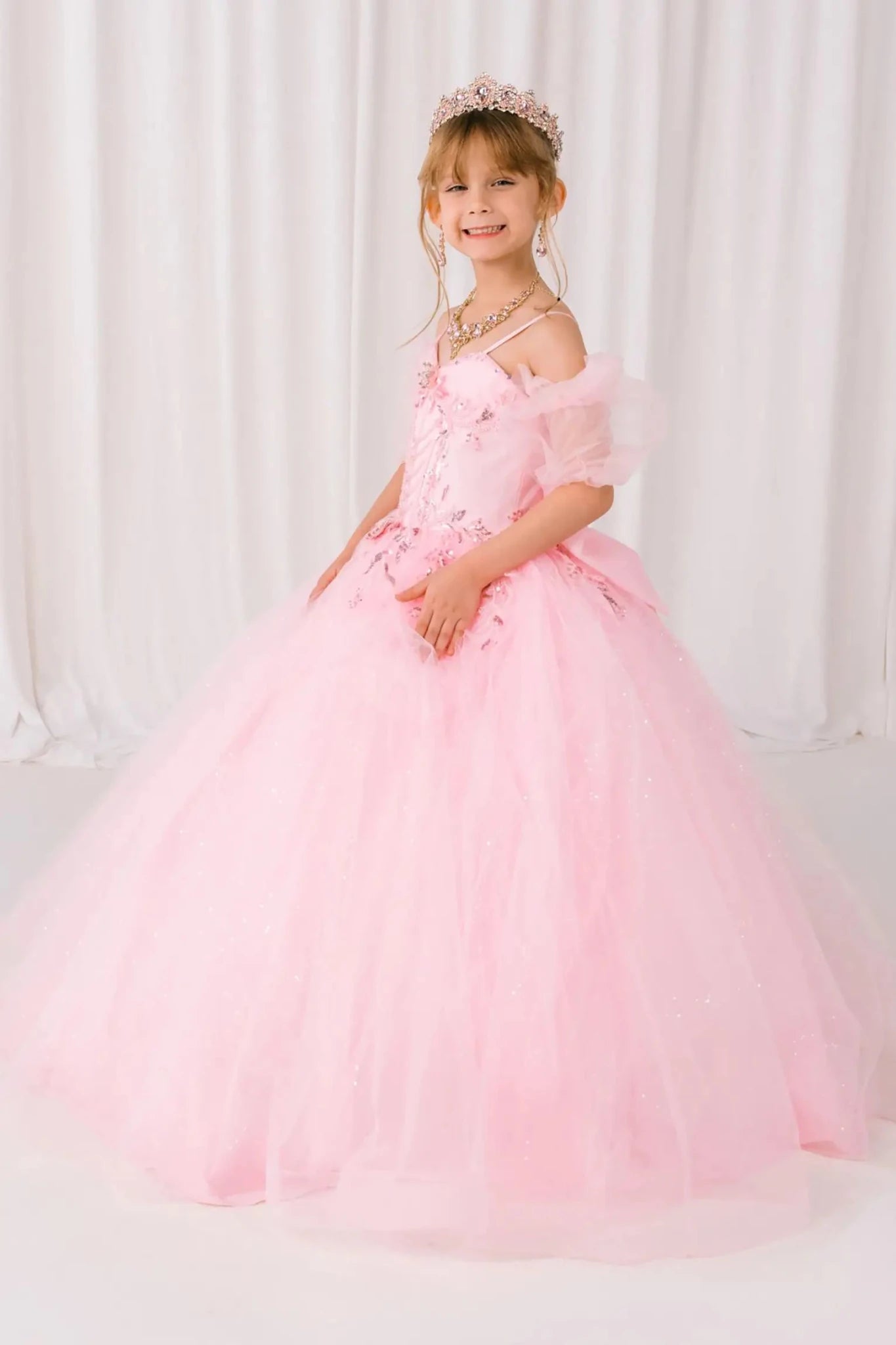Young girl standing side-facing in burgundy mini quinceañera ball gown with beaded floral bodice, draped details, sparkling tulle skirt, and layered silhouette