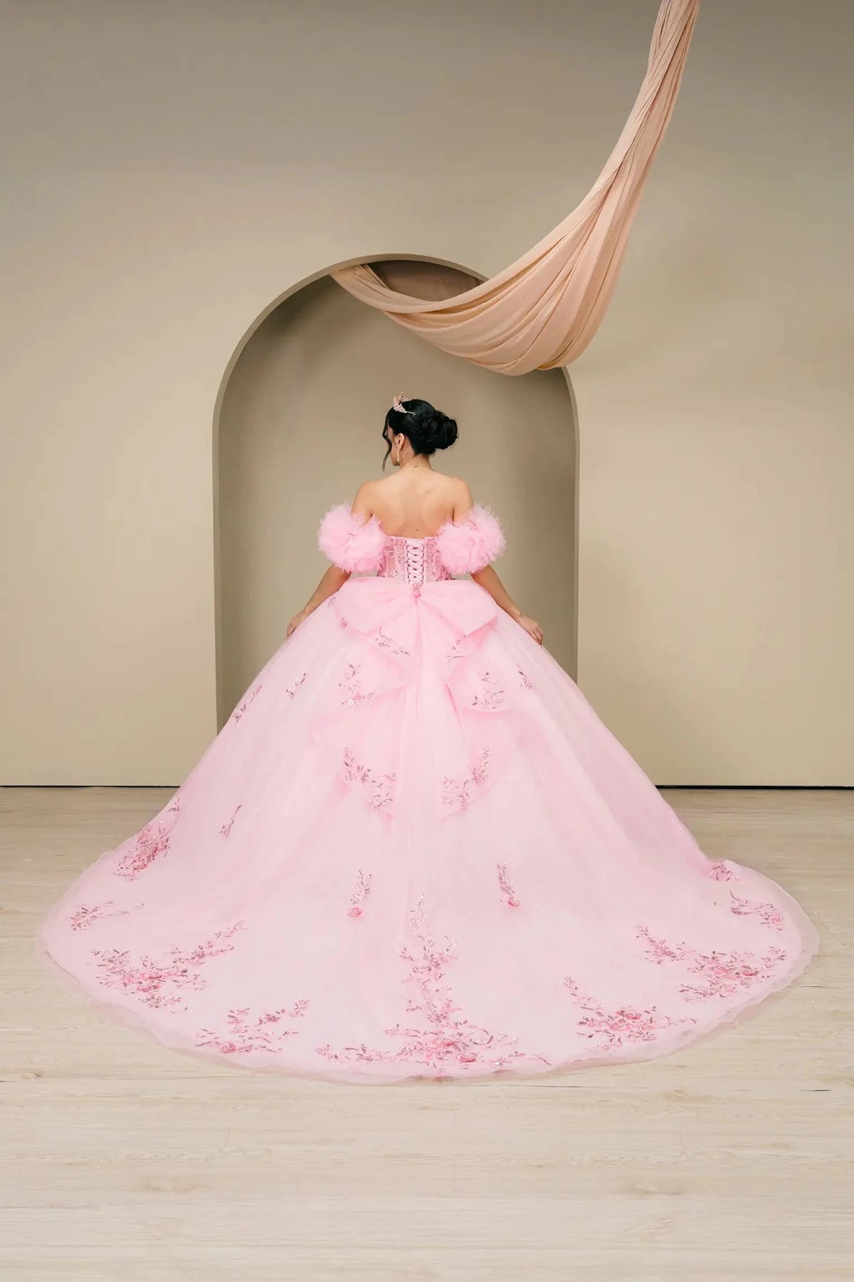 Full-length view highlights a pink quinceañera ball gown highlighting the extended train and embroidered hem.