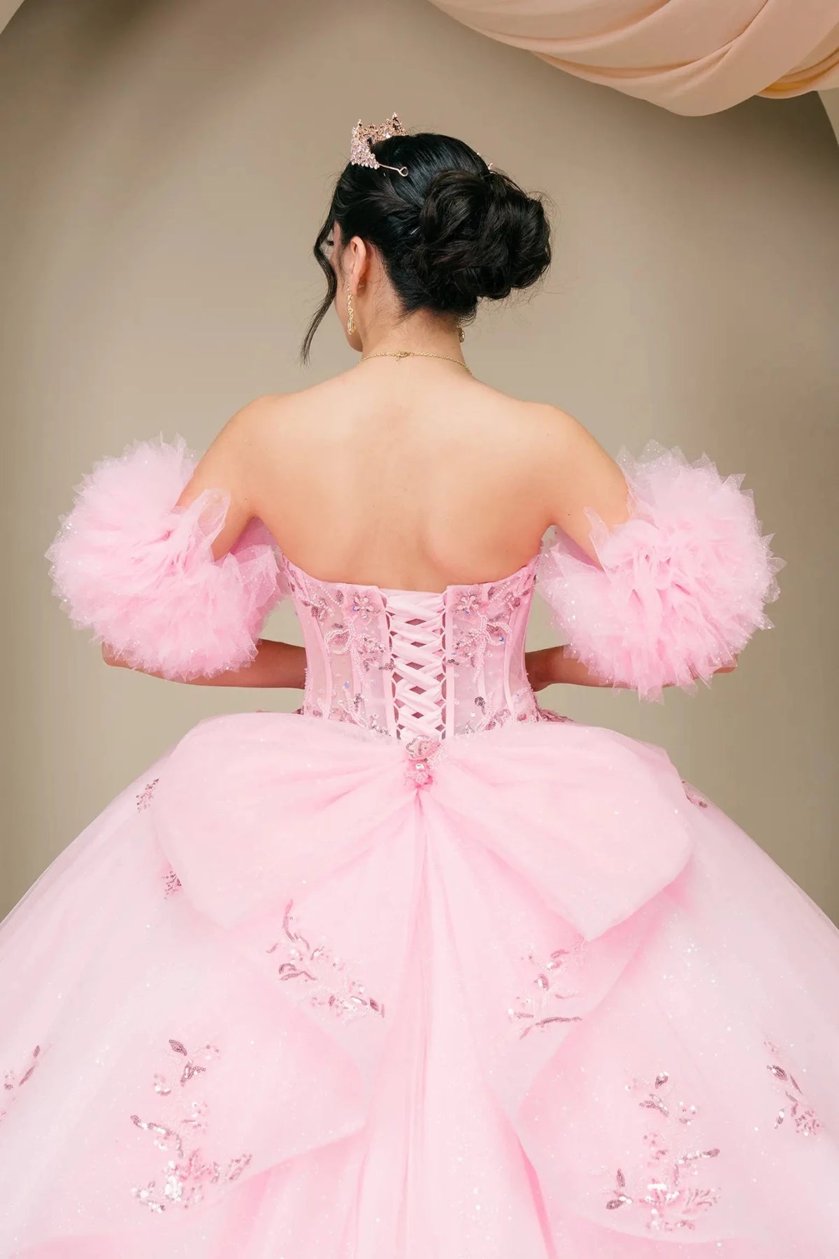 Back detail shows the pink gown showing lace-up corset back, puff sleeves, and bow accent.