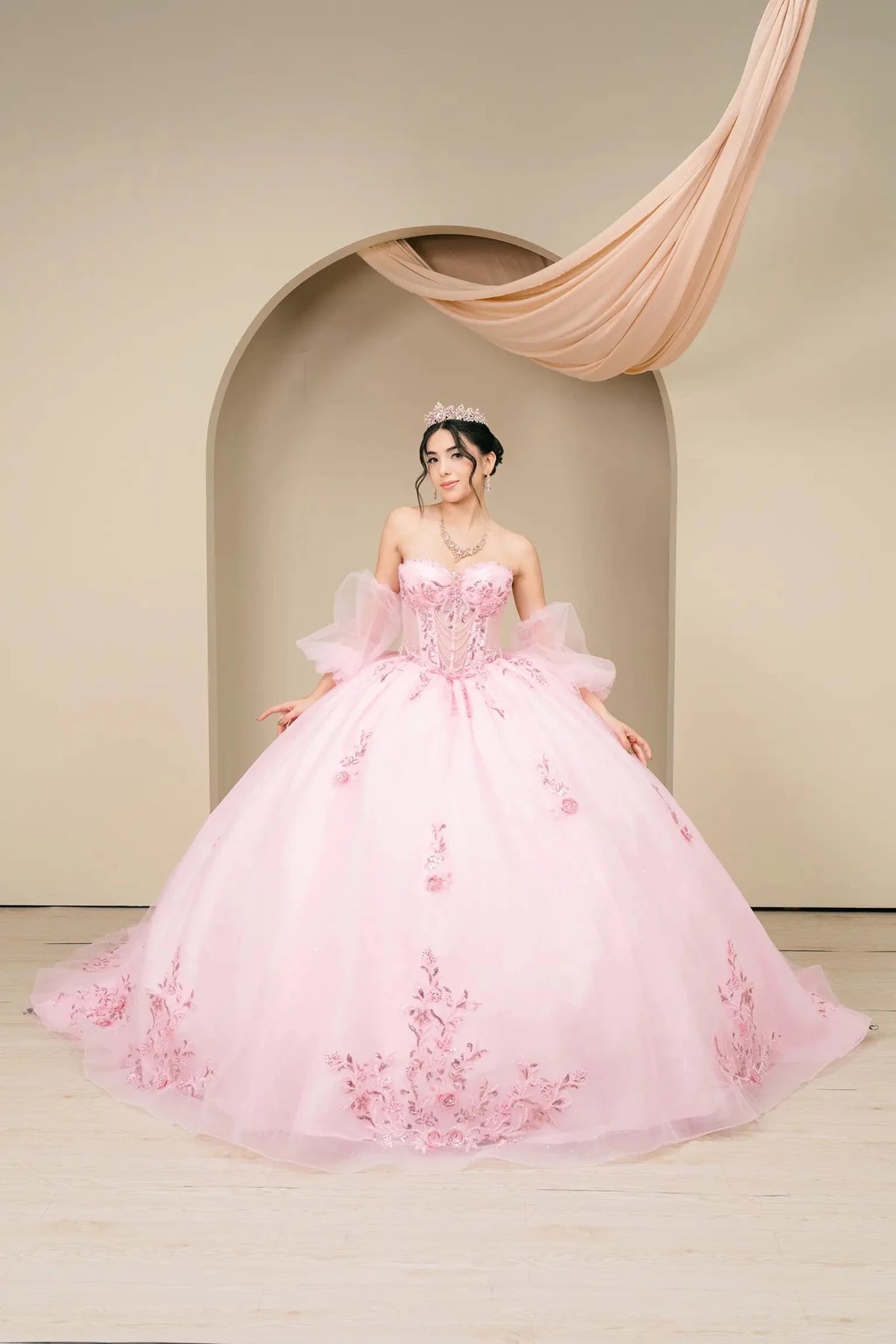 Front view presents a pink off-shoulder quinceañera ball gown with fitted corset and voluminous skirt.