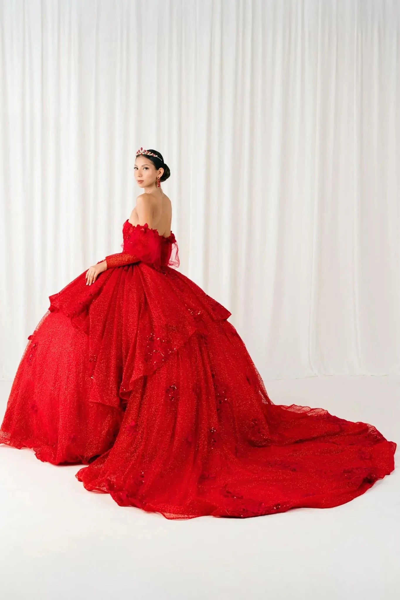 Side full view of a woman wearing red quinceañera dress highlighting detachable tulle sleeves, floral bodice details, and layered glitter tulle skirt.