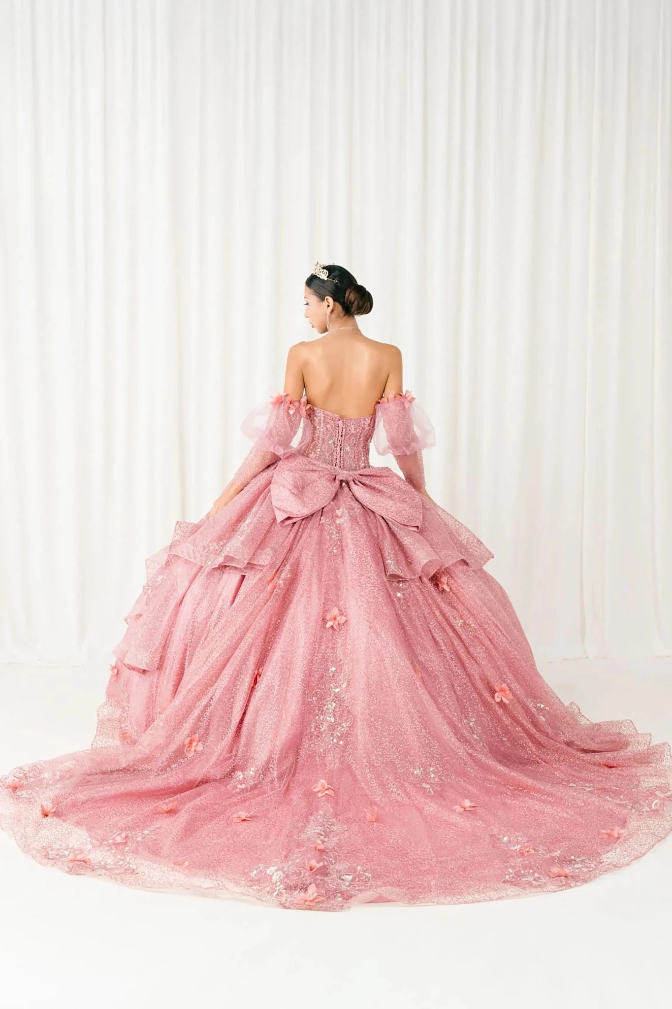 Back full-length view of Dusty Rose quinceañera ball gown with off shoulder tulle sleeves, sweetheart sequin bodice, layered glitter tulle skirt, and cathedral train