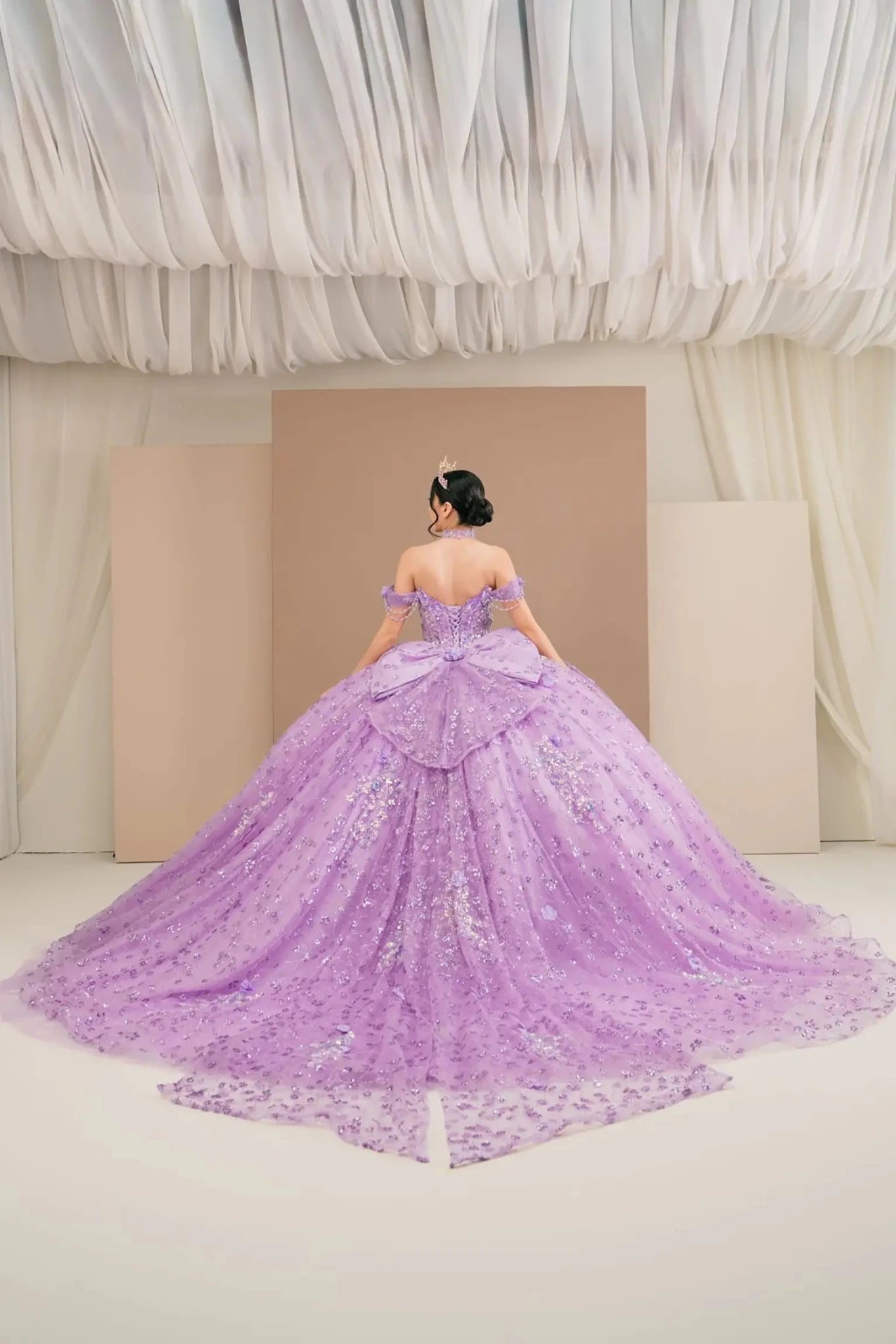 Back view of a woman wearing lilac quinceañera dress with voluminous glitter tulle skirt floral applique accents.