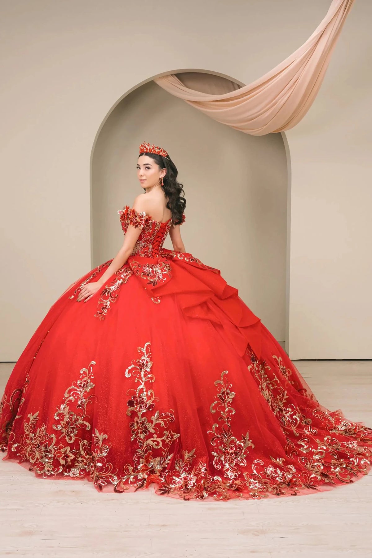 Detailed view highlights red quinceañera ball gown with off shoulder bodice, gold embroidery, floral appliqués, voluminous tulle skirt.