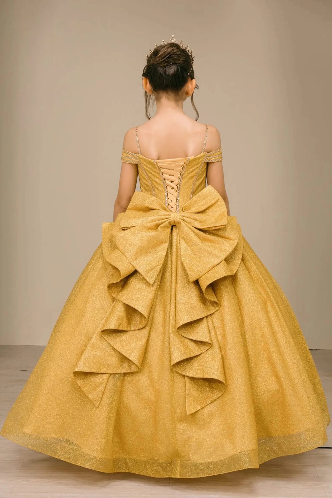 Close-up front-facing view of gold ball gown with embellished bodice and oversized tiered bow accent