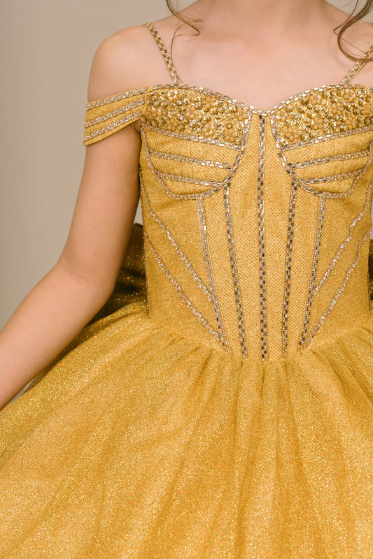Kid standing side-facing in gold ball gown with oversized tiered bow detail, shimmering bodice, and flowing layered skirt