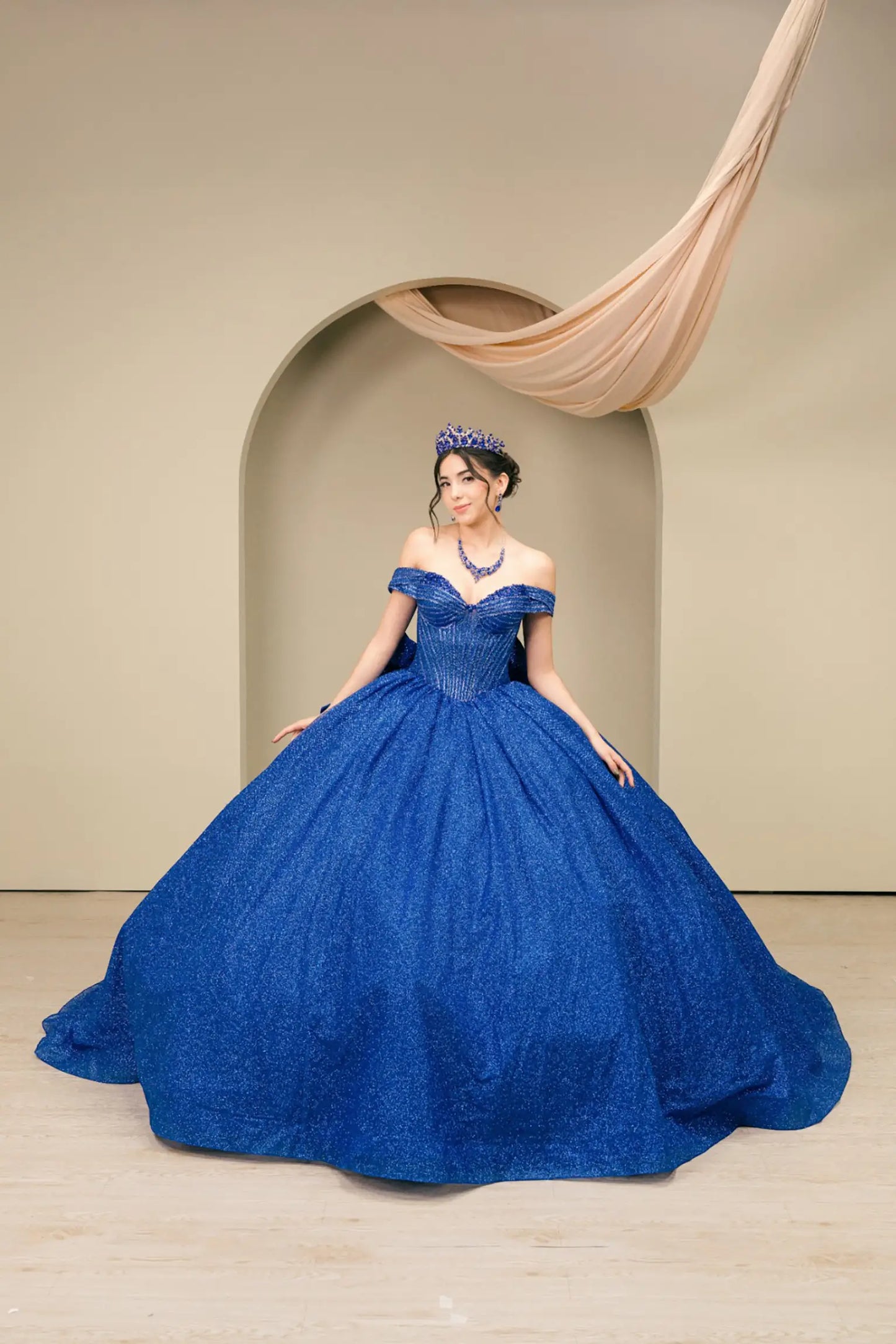 Woman standing front-facing in elegant royal blue ball gown with beaded corset bodice and voluminous glitter tulle skirt
