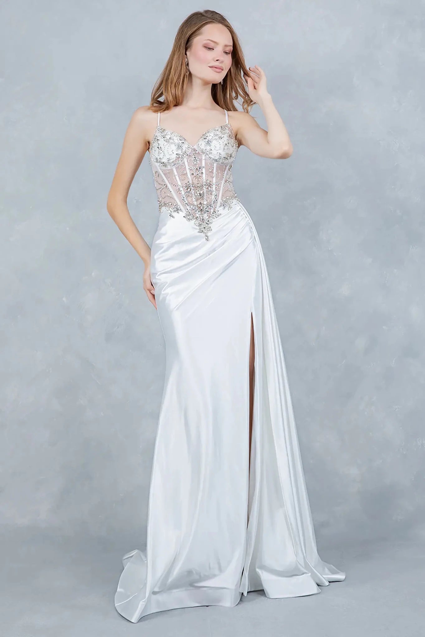 A full-length front view of a woman wearing a silver formal prom dress with a lace-up corset and train.
