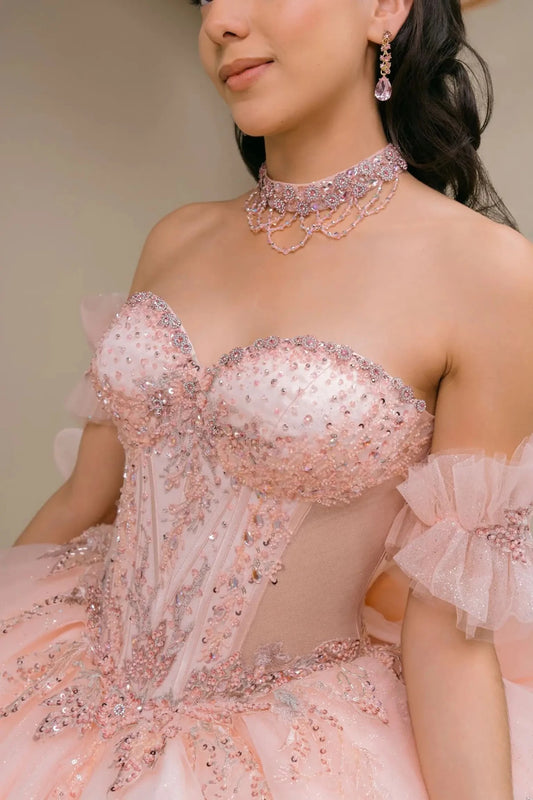 Close-up of woman wearing blush off-shoulder sweetheart quinceañera dress with beaded corset bodice, floral appliqué, and sweetheart neckline