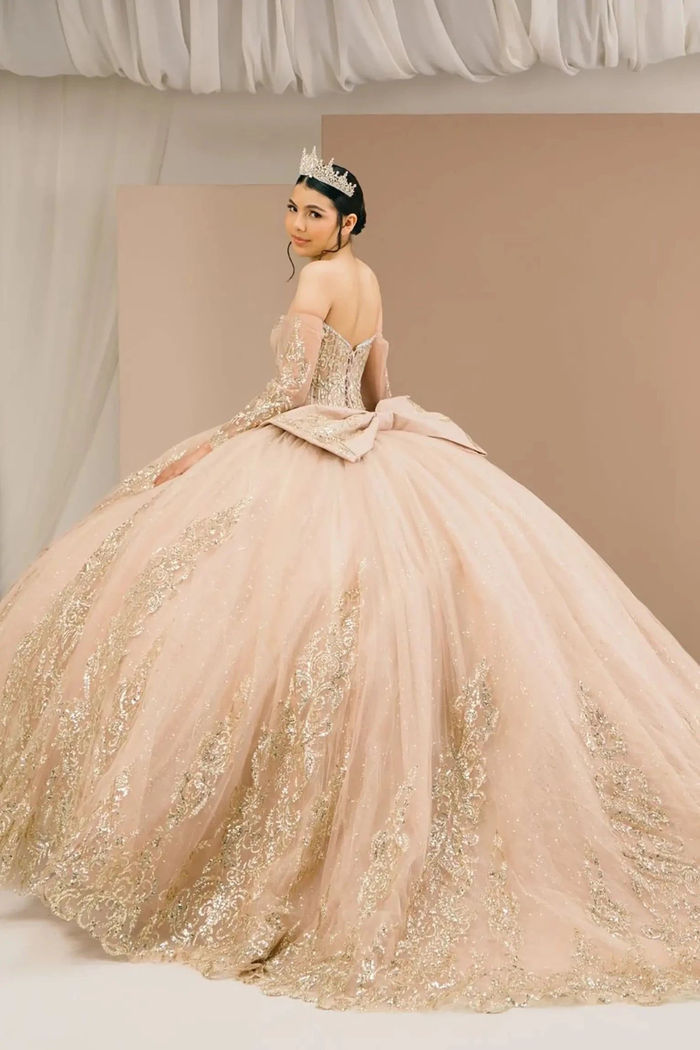 Back full view of a woman wearing mocha quinceañera dress with voluminous layered skirt, lace-up corset closure, and gold embroidered accents.