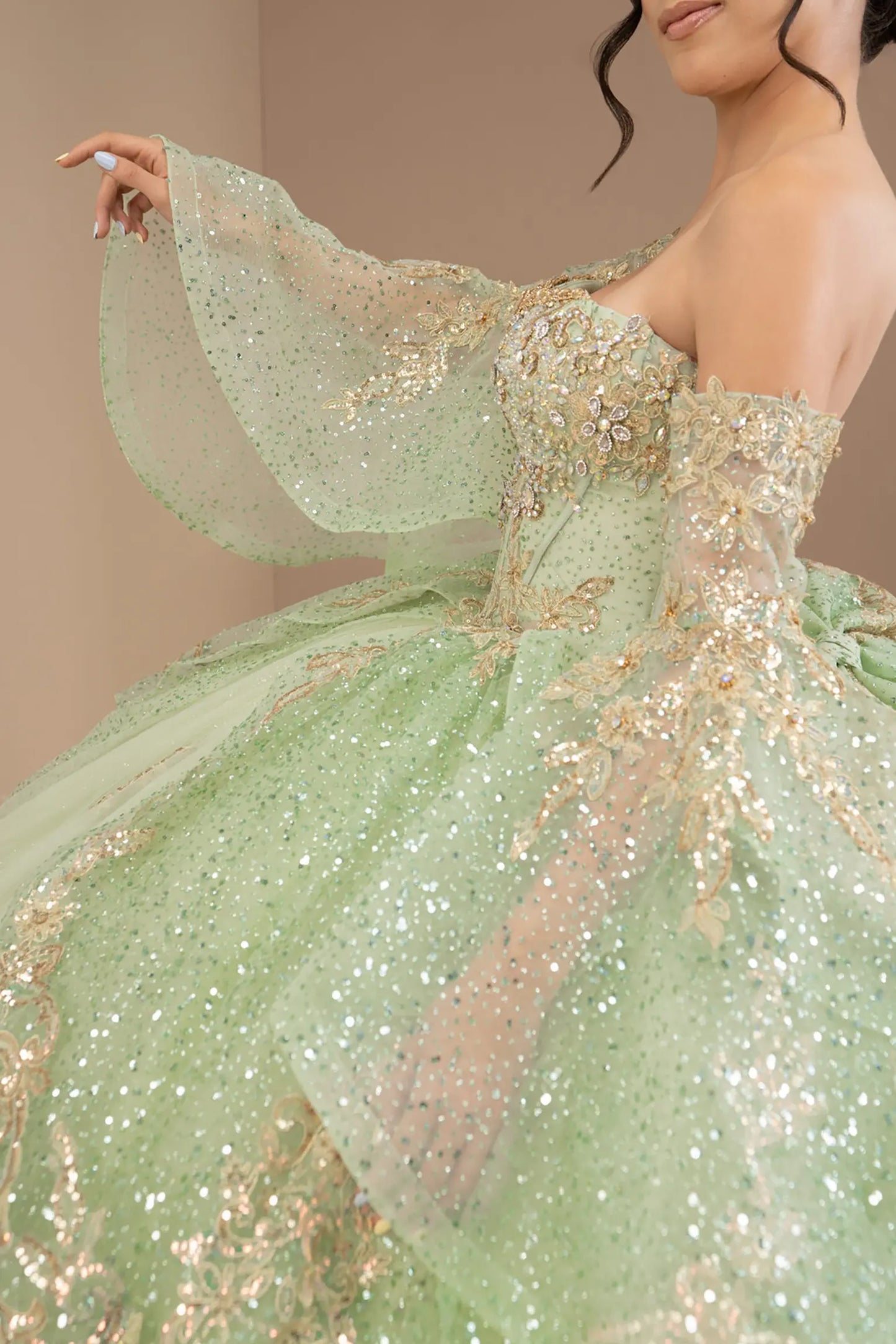 Side close-up view of a woman wearing sage quinceañera dress highlighting layered glitter tulle, embroidered bodice, and flowing ball gown silhouette.