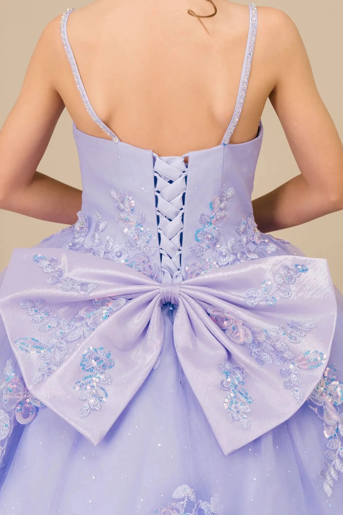Bodice back close-up of a kid wearing lilac mini quinceañera dress showing floral appliques, butterfly bow detail, and subtle glitter accents and glitter accents lace back up