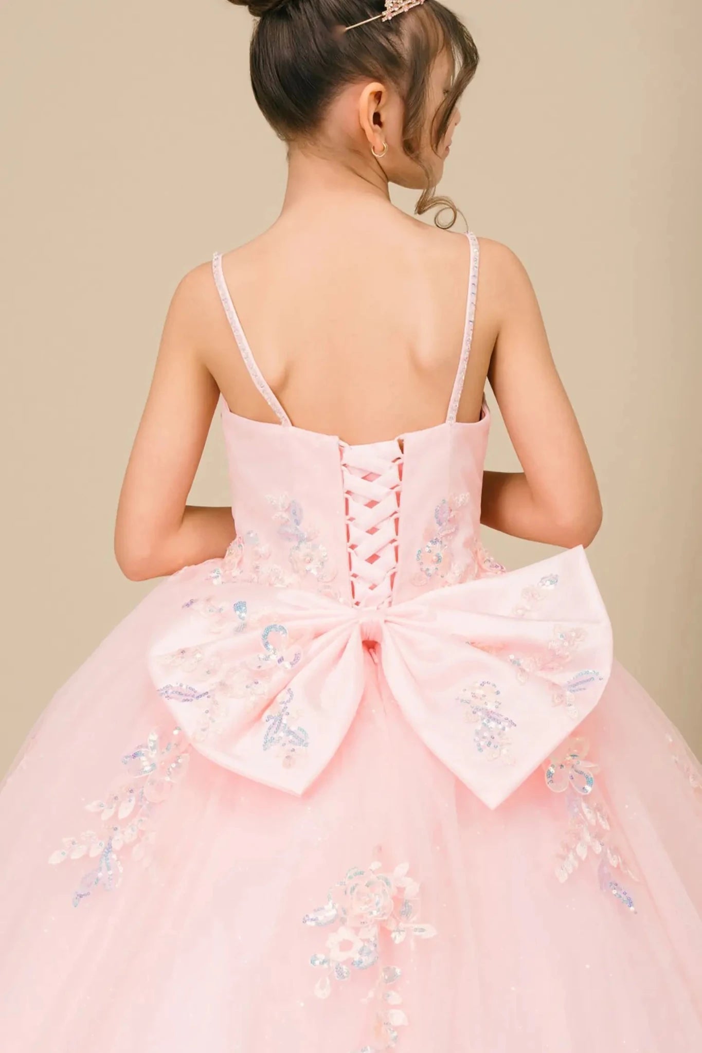 Bodice back close-up of a woman wearing pink mini quinceañera dress showing floral appliques, butterfly bow detail, and glitter accents lace back up