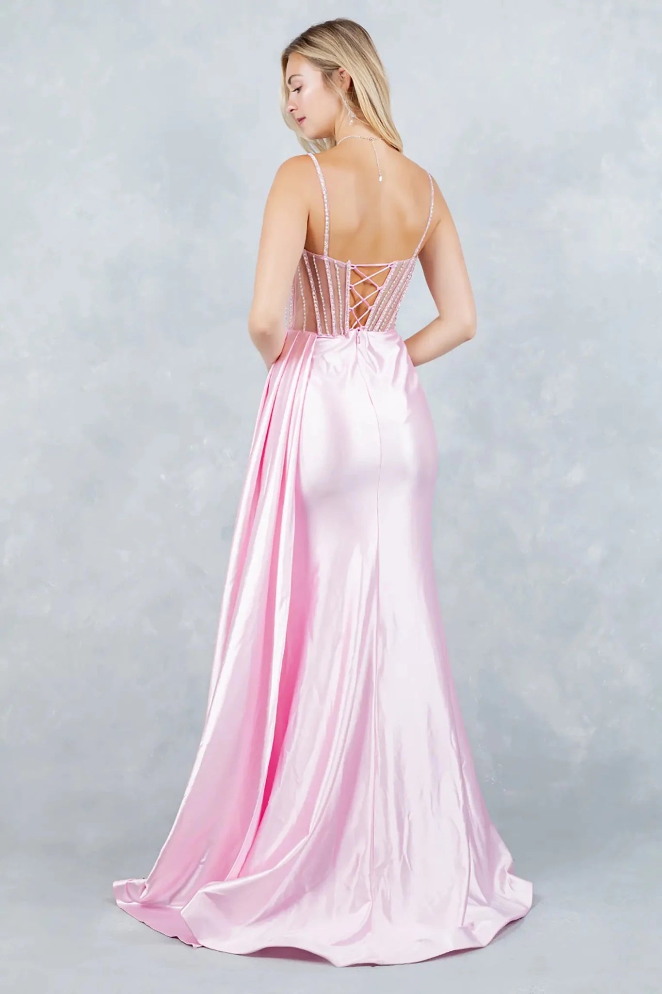 A full back view of a woman wearing a pink satin dress with a lace-up corset closure.