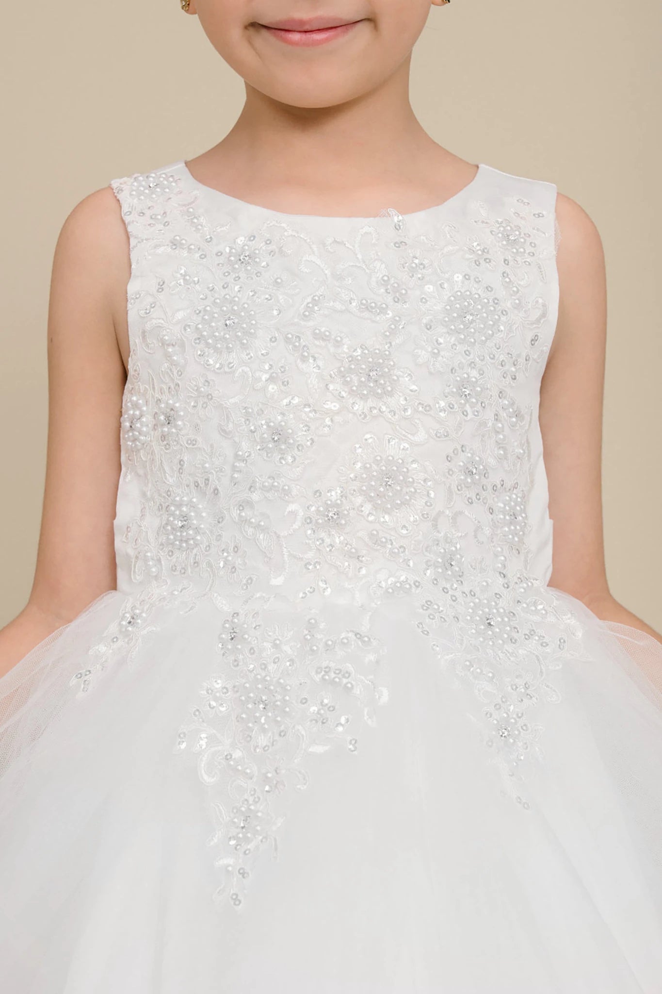 Close-up front-facing view of white sleeveless high-low tulle flower girl dress with lace bodice, pearl trim neckline, and rhinestone detailing.