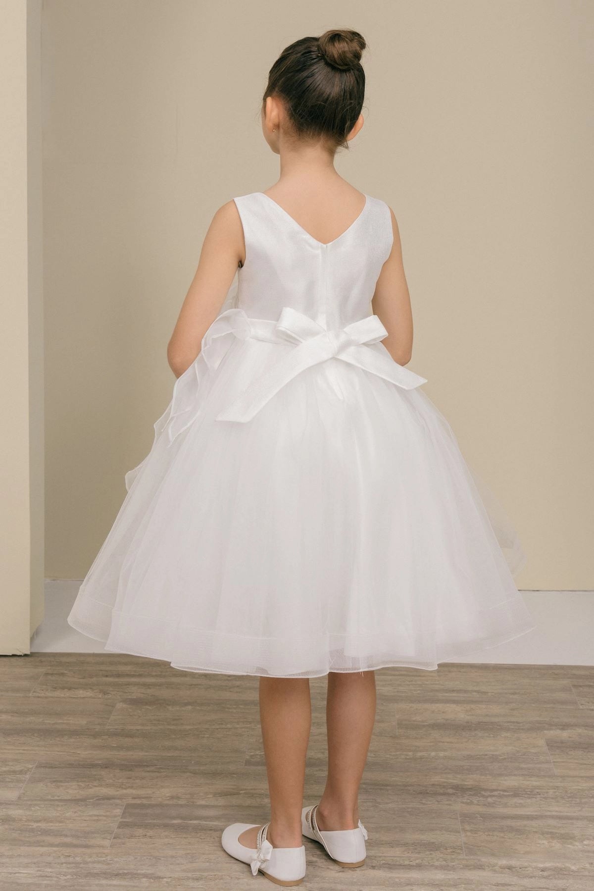 A White flower girl dress showing satin back bow above the layered skirt.