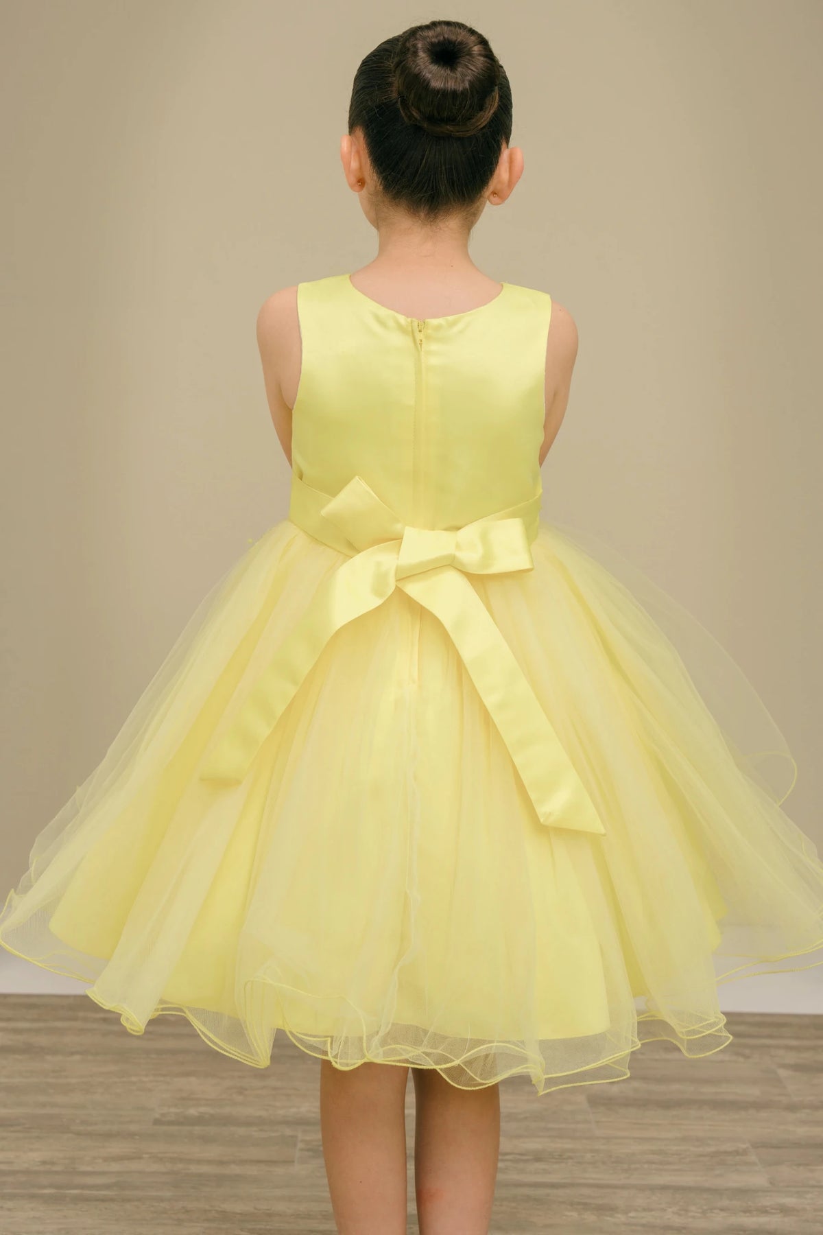 Displayed in a back view, the Yellow flower girl dress has zipper back and satin bow above the layered tulle skirt.