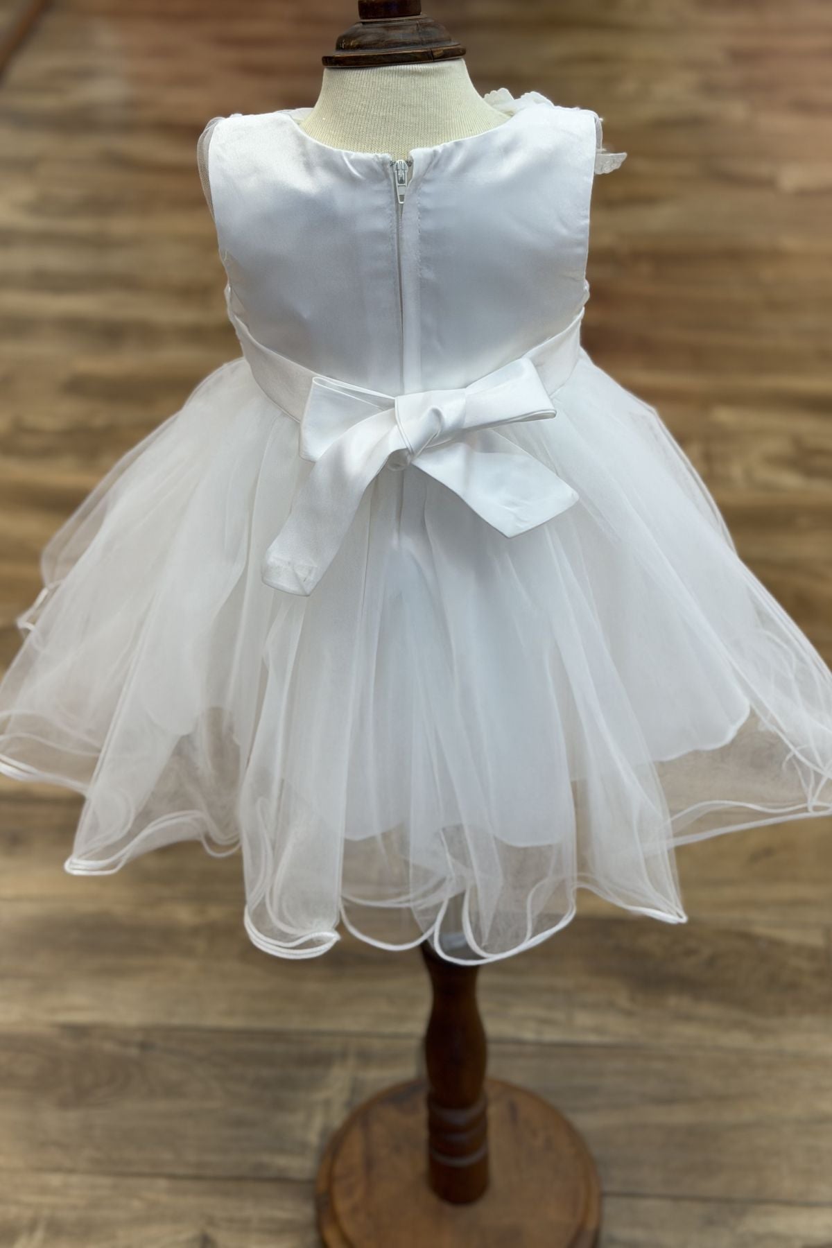 White flower girl Dress Front View With Layered Skirt And Oversized Bow Detail.
