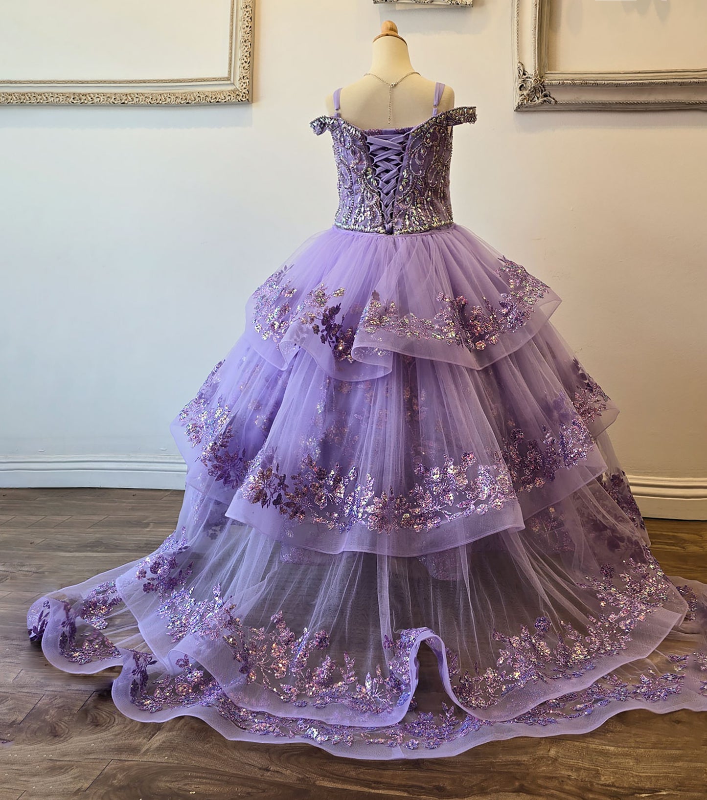 Purple ball gown with floral embellishments on a mannequin against a neutral wall.