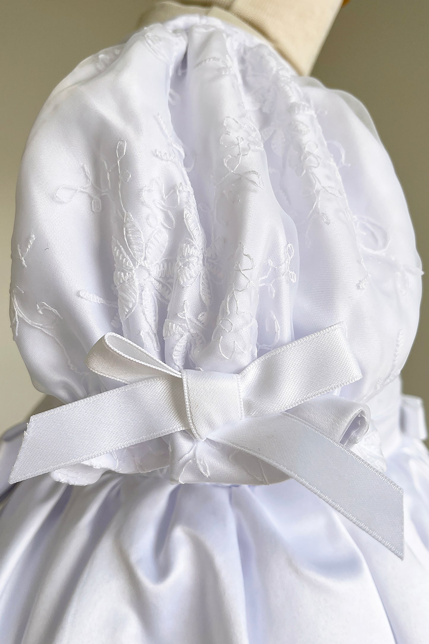 White satin dress with lace details and a large bow on a mannequin against a neutral background