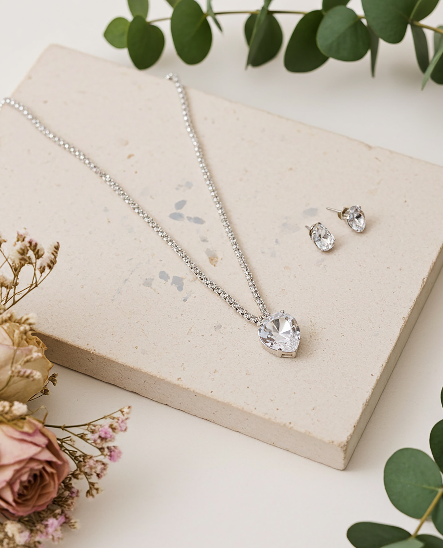 Silver necklace and earrings on a textured surface with flowers and leaves.