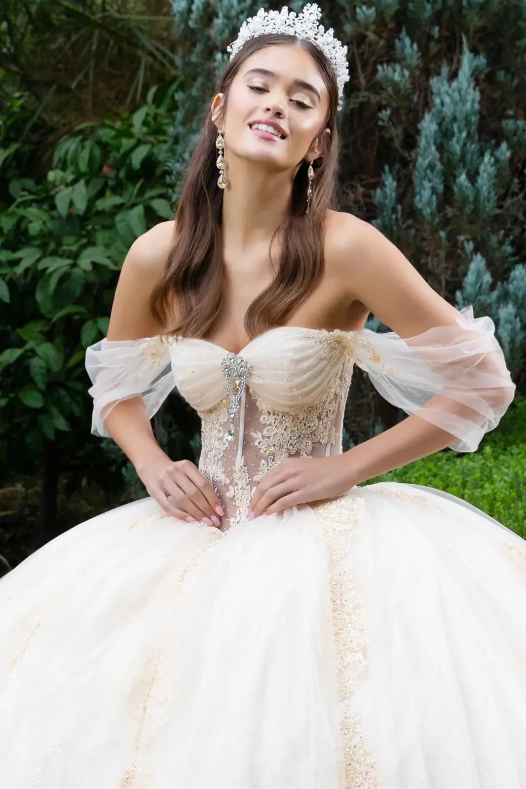 Front zoom view of a woman wearing champagne quinceañera dress with sheer bodice, glitter mesh skirt, lace detailing, corset structure