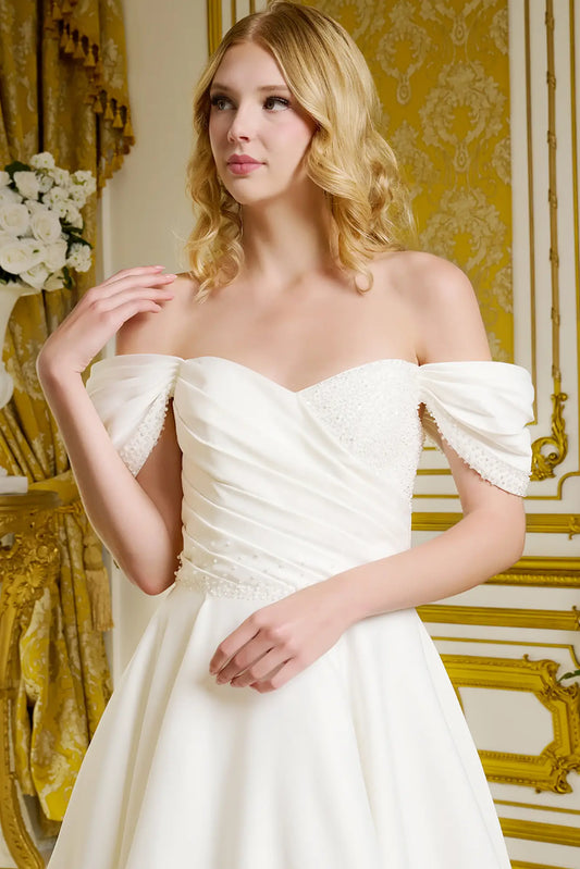 Woman wearing a white off-shoulder dress in an ornate room with gold accents.