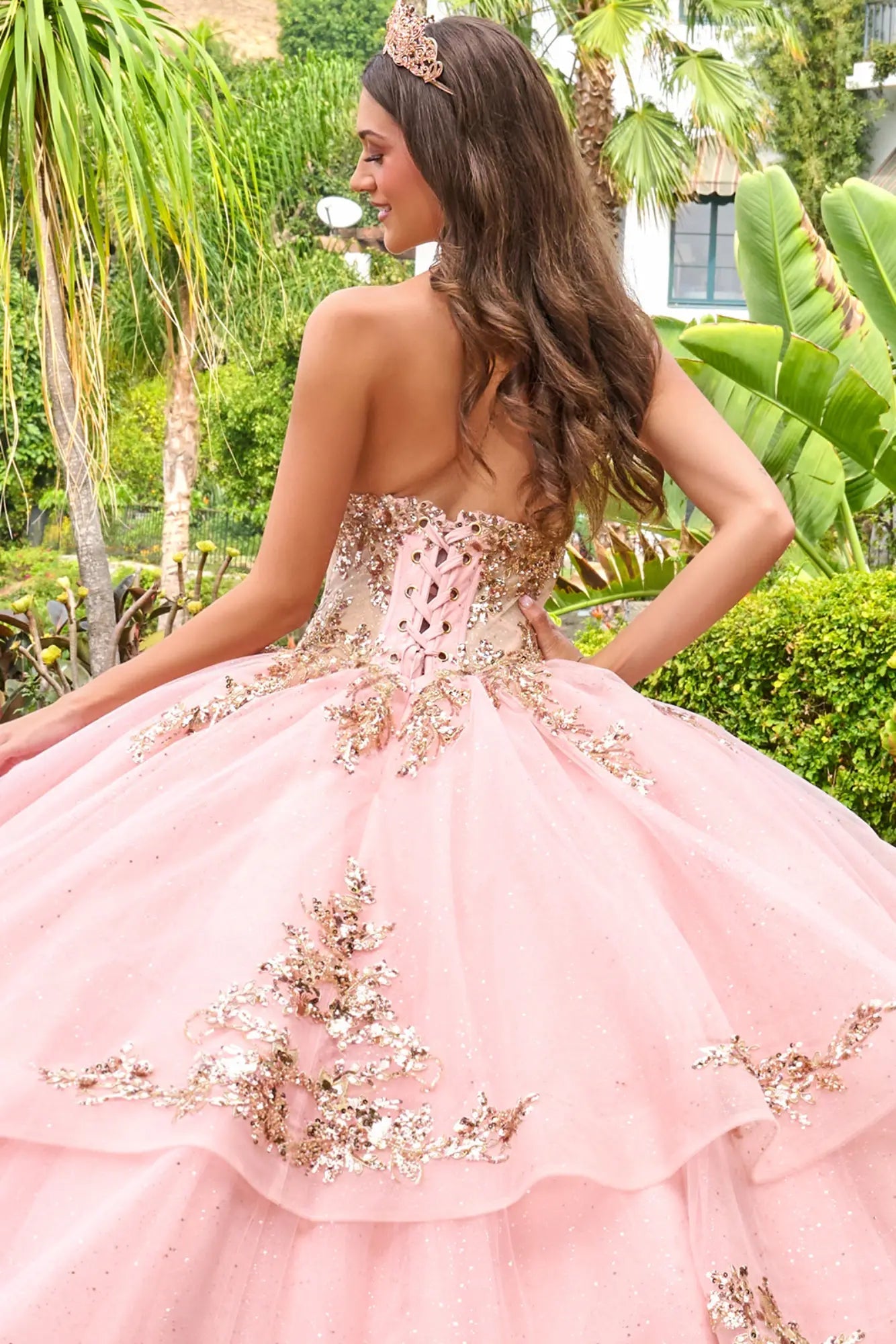 Close-up back detail of blush pink quinceañera ball gown featuring lace-up corset closure and embroidered appliqués on layered tulle skirt