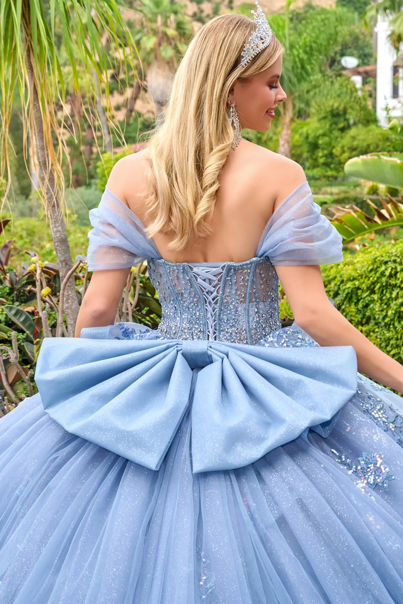 Close-up back detail of dusty blue quinceañera gown with lace-up corset, off-the-shoulder sleeves, and large bow accent