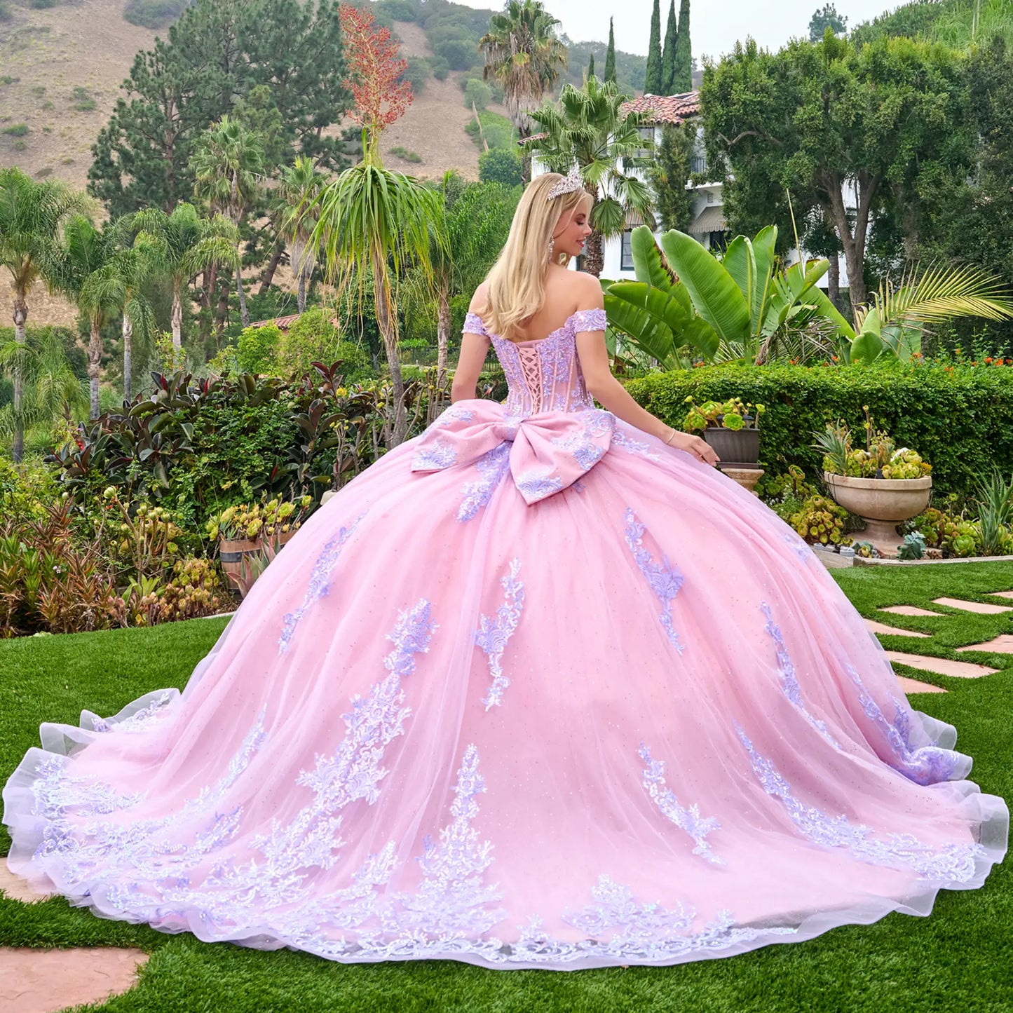 Angled back view of a woman wearing lilac quinceañera dress lace-up corset oversized bow embroidered tulle skirt