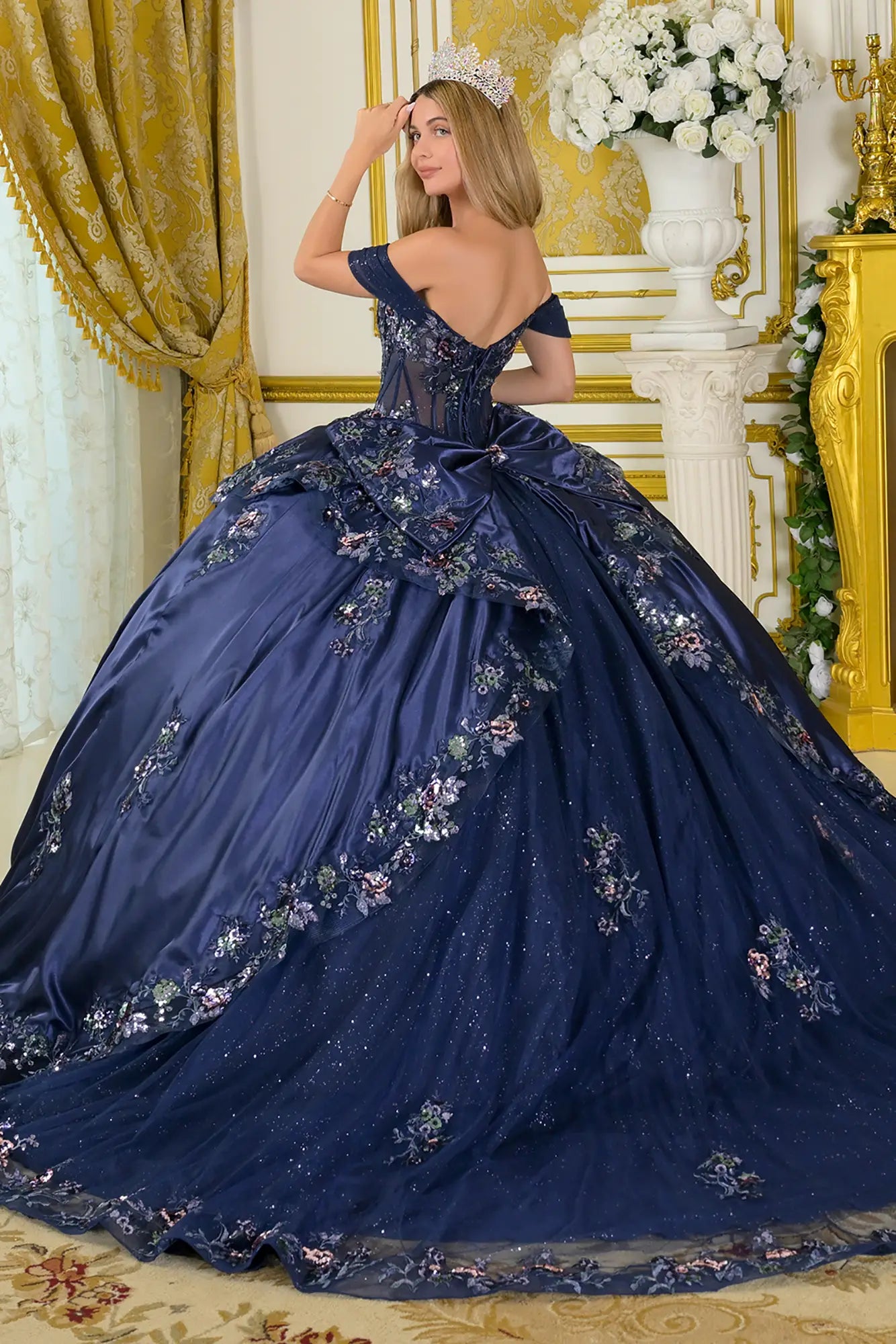 Girl wearing a navy quinceañera dress with satin-decorated bodice in a decorated room.
